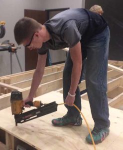Students in Woonsocket School’s Industrial classses have begun building the stage for the Theater Project at the community center. Above, Ryan Poyer nails the flooring down for the stage.