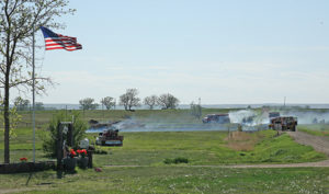 A FLAG flies in the yard of Glenn Hohn of rural Alpena, as members of the Woonsocket Fire Department extinguish a small grassfire, which apparently spread from a burn pile. The wind was blowing in the right direction to spread the fire away from the home, but firemen had the fire in hand before it went far, anyway.